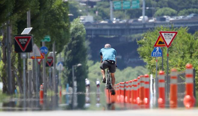 전국적으로 35도 내외의 찜통더위가 계속된 26일 서울 송파구 한강공원을 찾은 시민이 지열로 아지랑이가 피어오르는 자전거도로를 지나고 있다. 연합뉴스