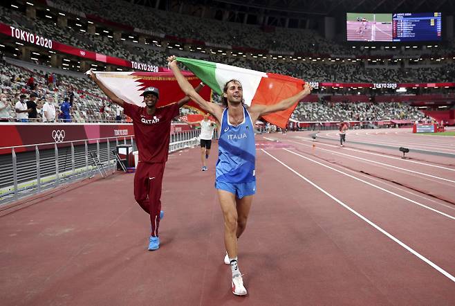 카타르의 무타즈 에사 바르심(왼쪽)과 이탈리아의 지안마르코 탐베리가 지난 1일 일본 도쿄 올림픽스타디움에서 열린 육상 남자 높이뛰기 결선에서 공동금메달이 결정된 후 함께 자국기를 들고 트랙을 돌고 있다. AP 연합뉴스