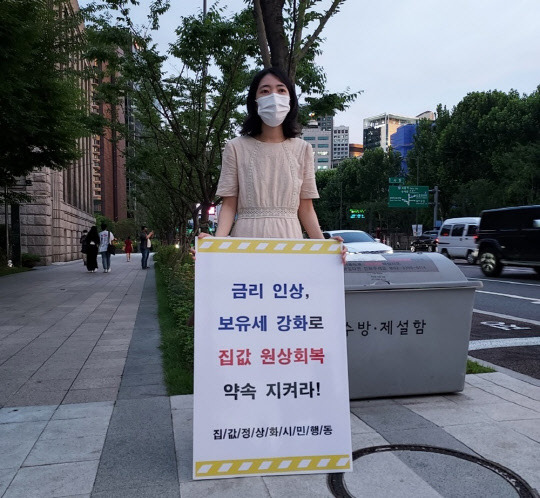 집값정상화시민행동의 한 회원이 지난 6일 오후 서울 청계천 일대에서 '금리 인상, 보유세 강화로 집값 원상회복 약속 지켜라'라는 피켓을 들고 1인 시위를 하고 있다. <집값정상화시민행동 제공>