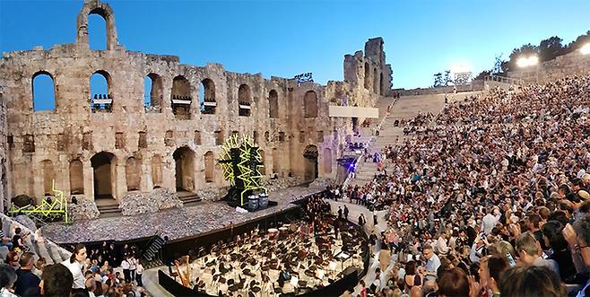 아크로폴리스 아래, 로마 지배 시기에 세워진 고대 극장 ‘헤로데스 아티쿠스 오데온’에서 오페라 노르마가 공연되고 5000석을 가득 채운 객석에는 기대감과 설렘이 감돈다.
