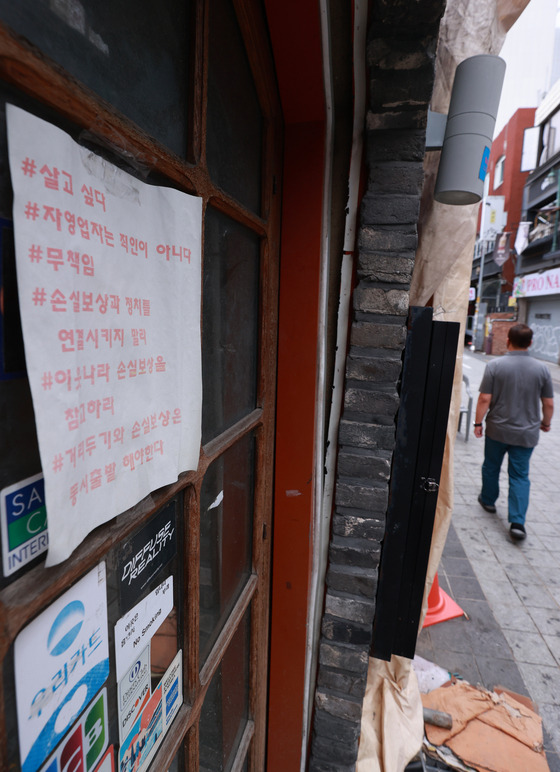 A sign condemning the government's Covid-19 social distancing measures is on display at the front of a restaurant in Itaewon, central Seoul, on Monday. According to an emergency committee of self-employed business owners, a drive-through protest that calls for eased social distancing restrictions is scheduled in nine cities on Wednesday night. [YONHAP]