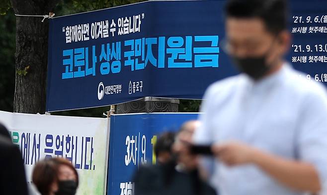 지난 6일 서울 중로구 도심에서 시민들이 '코로나 상생 국민지원금' 신청 안내 현수막 앞을 지나고 있다. 뉴시스
