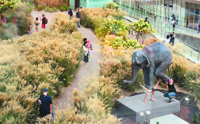 롯데백화점 동탄점 3층과 연결돼 있는 3300㎡의 힐링 공간 '더 테라스'는 국내 최대 규모의 야외 정원이다. 실제 갈대밭이 조성돼 있다. 사진 오른쪽 아래는 코끼리의 무게를 견디는 남자를 묘사한 현대미술가 파비앙 머렐의 작품 '펜타튜크'.