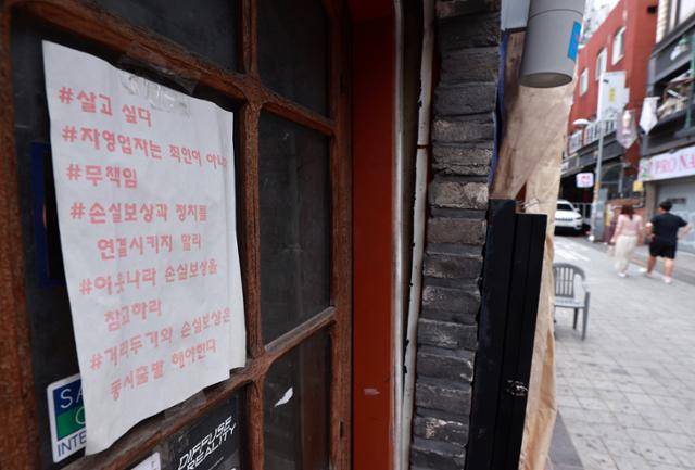 6일 서울 용산구 이태원의 한 휴업 가게 출입문에 비에 젖고 햇빛에 바랜 자영업자 시위 문구가 적힌 종이가 부착돼 있다. 이 문구들은 신종 코로나바이러스 감염증(코로나19) '4차 대유행' 이후 사회관계망서비스(SNS) 등을 통해 확산됐던 자영업자들의 온라인시위 관련 해시태그들이다. 연합뉴스
