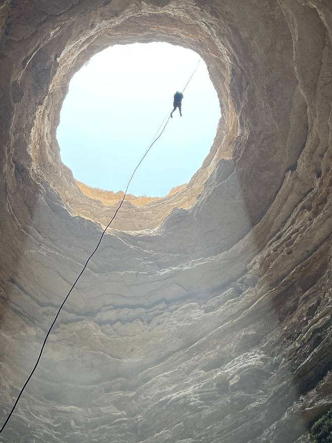오만 동굴탐사팀이 공개한 ‘바르호우트의 우물’ 사진. 탐사대원 한명이 밧줄을 타고 내려오고 있다. 탐사팀은 동굴 깊이가 약 112m 정도고 폭은 30m라고 밝혔다./AFP 연합뉴스