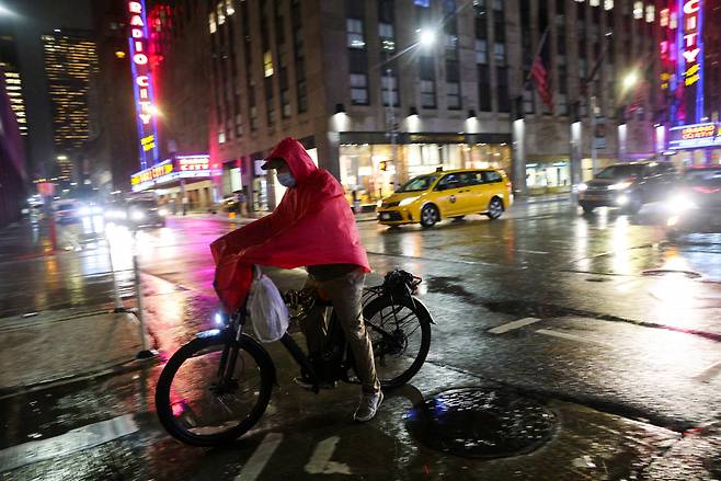 한 배달 노동자가 23일(현지시간) 미국 뉴욕시 맨해튼 시내에서 우비를 뒤집어 쓰고 배달을 하고 있다. [로이터]
