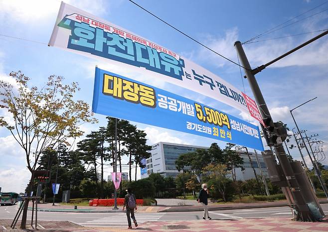 24일 경기도 성남시청 인근 교차로에 성남 대장동 개발 사업과 관련해 더불어민주당 소속 경기도의회 의원과 국민의힘 지역 당협위원장 이름으로 상반된 의미를 담은 현수막이 함께 걸려 있다. 현수막 너머로 성남시청의 모습이 보이고 있다. [연합]