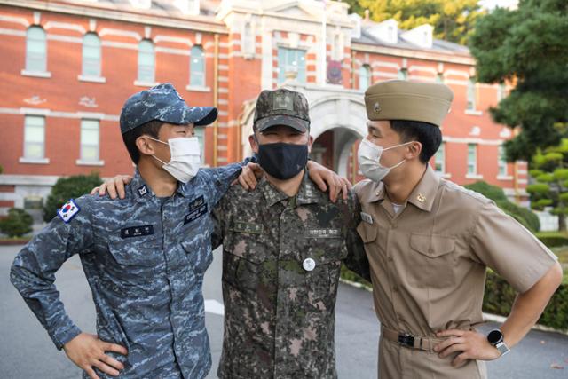 해군 김희민(왼쪽), 김성민(오른쪽) 하사가 진해기지사령본부 건물 앞에서 아버지 김동환 중령과 어깨를 나란히 걸고 환하게 웃고 있다. 해군 진해기지사령부 제공