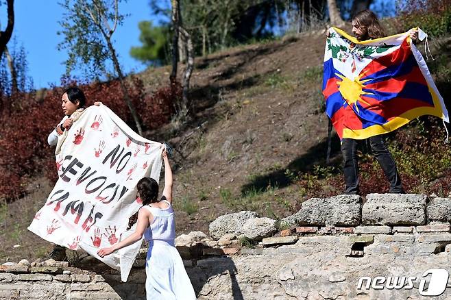 베이징 동계올림픽 성화 채화식장에 난입한 운동가들이 티베트 깃발과 학살 중단이라 쓰인 배너를 펼쳐 보이고 있다. © AFP=뉴스1