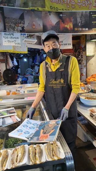 Lee Bok-soo, the 71-year-old owner of Namkyung Banchan, a side dish shop in Mangwon Market, Mapo District, western Seoul, shows photographs of customers who use reusable containers to cut down on plastic waste on Oct. 10. The traditional market is currently holding a campaign to encourage people to bring their own containers. [SARAH KIM]