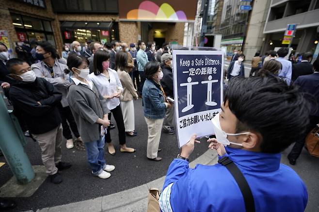 코로나19 대유행으로 인해 마스크를 눌러쓴 일본 시민들이 21일 도쿄에서 진행 중인 자민당의 선거 유세 장면을 지켜보고 있다. 한 선거운동원이 “일정 거리를 유지해달라”는 표지판을 들고 있다. 도쿄 연합뉴스