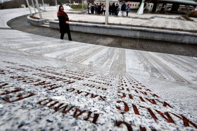 2019년 3월 보스니아 동부 스레브레니차 포토카리 추모센터에서 한 이슬람계 여성이 희생자들의 이름이 적힌 추모벽을 지나고 있다. 보스니아 내전 말기인 1995년 7월 세르비아군이 보스니아 이슬람교도를 상대로 벌인 스레브레니차 집단학살로 8,000명의 민간인이 목숨을 잃었다. 스레브레니차=AFP 연합뉴스 자료사진