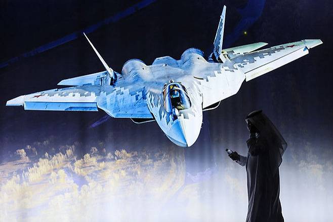 지난 14일(현지시간) 아랍에미리트에서 열린 두바이 에어쇼에서 러시아 전투기 제조사인&nbsp;UAC 부스에 설치된 SU-57 스텔스 전투기 영상을 현지인이 지나고 있다. 연합뉴스