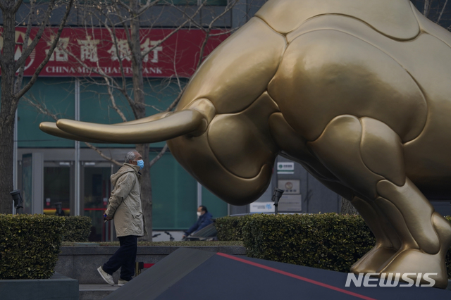 [베이징=AP/뉴시스] 11일 중국 베이징 도심에서 한 남성이 황소 동상 옆을 지나가고 있다. 2021..03.11