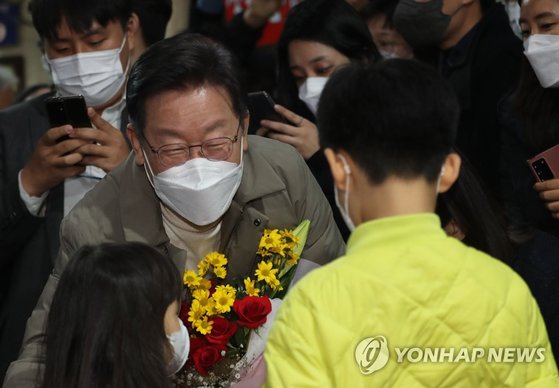 이재명 민주당 대선 후보와 부인 김혜경 씨가 12일 경북 김천 황금시장을 방문해 어린이들로부터 환영 꽃다발을 받고 있다. 연합뉴스