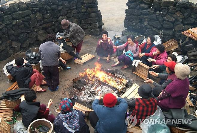 몸 녹이는 해녀들 (제주=연합뉴스) 해녀들이 물질을 가기 전 불턱에 모여앉아 몸을 녹이고 있다. 2016.11.30 [제주특별자치도 해녀박물관 제공=연합뉴스] jihopark@yna.co.kr