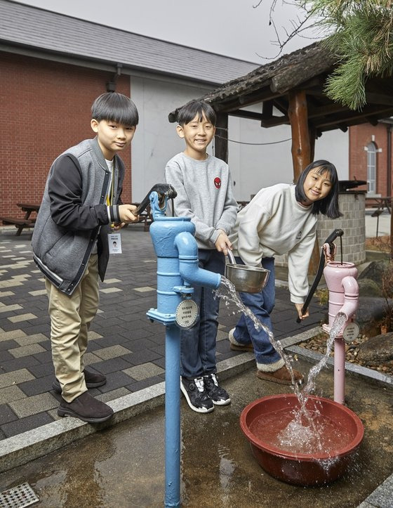 김휘윤 학생모델과 최주영 학생기자, 노윤채 학생모델(왼쪽부터)이 물 한 바가지를 펌프에 넣고 작두를 움직이면 물이 밑에서 쏟아져 나오는 작두 펌프를 직접 조작해봤다. 지금의 꼭지만 틀면 콸콸 나오는 수돗물과는 다른 형태다.