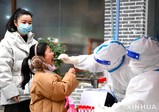 [정저우=신화/뉴시스] 최근 코로나19가 다시 급속히 퍼지는 중국 허난성 정저우에서 10일 한 어린이가 부모와 함께 시내 검사센터를 찾아 샘플 채취를 받고 있다. 2022.01.10