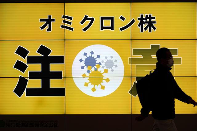 13일 일본 도쿄에서 한 시민이 코로나19 오미크론 변이 위험성을 알리는 화면 앞을 지나고 있다. 도쿄=AP 연합뉴스