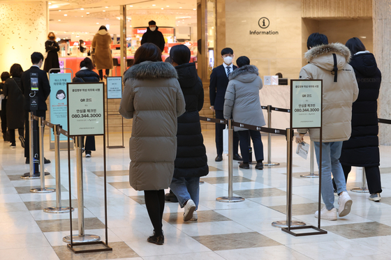 Visitors wait to show vaccine passes at the entrance of a department store in Seoul on Monday, one day before the vaccine pass program will be scrapped at six types of businesses nationwide, including department stores. [YONHAP]