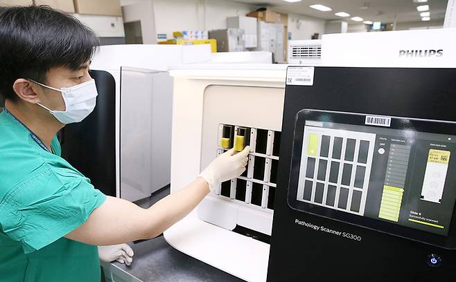 서울아산병원 병리 검사실 직원이 검체 슬라이드를 디지털 스캐너에 넣고 있다. 검체 슬라이드 스캔 영상은 서울아산병원 전자의무기록시스템(EMR)을 통해 자동 분류돼 담당 병리 판독 의사의 모니터로 전송된다. 서울아산병원 제공.