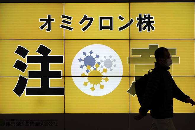 [도쿄=AP/뉴시스] 지난 13일 일본 도쿄에서 마스크를 쓴 한 남성이 오미크론 변이 주의를 알리는 대형 안내판 앞을 지나고 있다.