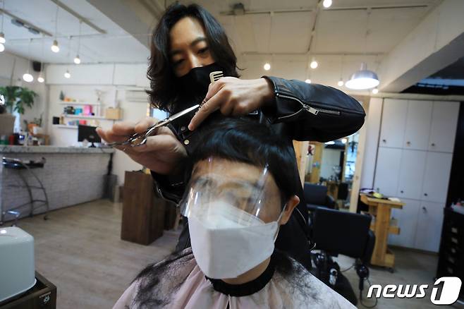 (서울=뉴스1) 구윤성 기자 = 20일 서울 마포구 라이언스타일 미용실에서 헤어디자이너가 고객에게 신종 코로나바이러스 감염증(코로나19) 예방을 위해 마스크와 페이스필름을 씌우고 커트를 하고 있다. 2020.3.20/뉴스1