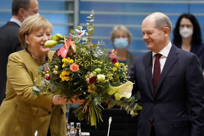 [베를린=AP/뉴시스] 앙겔라 메르켈 독일 총리가 24일(현지시간) 베를린 총리실에서 열리는 각료회의에 앞서 올라프 숄츠 부총리 겸 재무장관으로부터 꽃다발을 받아 들고 있다. 메르켈 총리는 지난 9월 선거 이후 새 내각을 구성하기 위한 마무리 협상이 진행 중인 가운데 이번 각료회의가 총리로서 마지막으로 여겨져 이 꽃다발을 받았다. 2021.11.24.