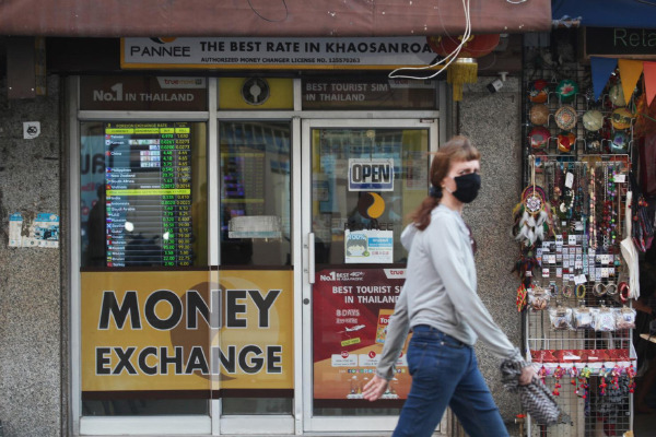 A woman walks past a currency exchange shop on Khao San Road in Bangkok. (Photo: Nutthawat Wicheanbut)