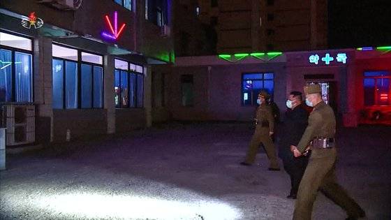 김정은 위원장이 약국을 찾아가는 길이 어둡다. 북한 군인이 김정은 앞쪽으로 휴대용 손전등을 비추고 있다.