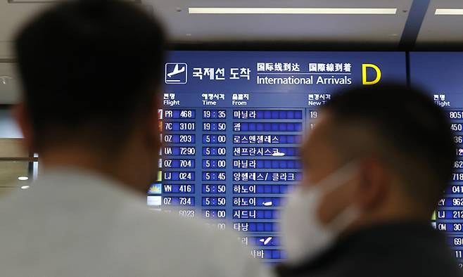 지난 19일 인천국제공항 입국장 전광판에 적혀있는 국제선 도착시간을 보고 있는 승객들. 연합뉴스