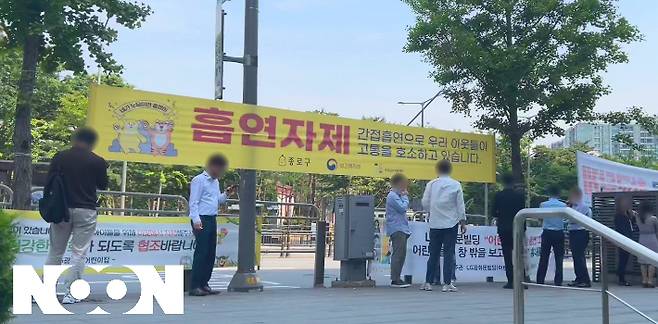 서울 종로구 LG광화문빌딩 앞 인도. '어린이집 앞 흡연 그만, 어린이들이 창 밖을 보고 흡연을 흉내냅니다'라는 내용의 현수막 앞에서 직장인들이 담배를 피우는 모습. [눈] 영상캡처