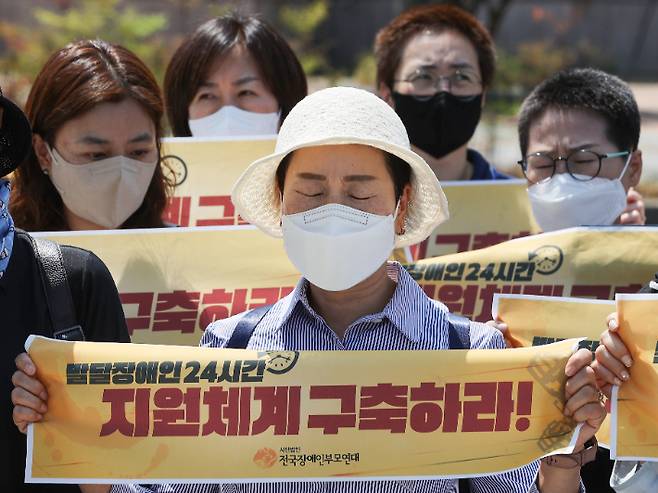 지난 31일 오전 서울 용산구 대통령 집무실 앞에서 열린 '49재 기간 집중투쟁 선포' 기자회견에서 한 참가자가 현수막을 들고 눈을 감고 있다.  이들은 지난 23일 숨진 발달장애인과 그 가족들의 49재가 끝나는 7월 10일까지 발달장애인 24시간 지원체계 구축을 위해 집중 투쟁하겠다고 밝혔다. 연합뉴스