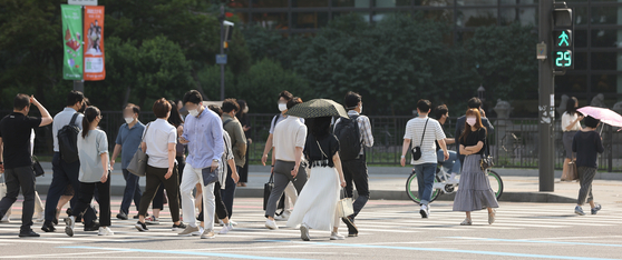 지난 21일 오전 서울 광화문역 인근에서 출근하는 시민들이 양산이나 손으로 햇빛을 가리며 길을 건너고 있다. 〈사진=연합뉴스〉