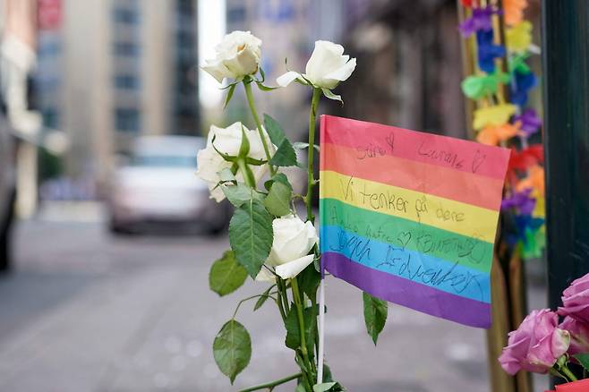 25일(현지시간) 노르웨이 오슬로에서 성소수자 축제를 앞두고 발생한 총기난사 사건으로 2명이 숨지고 21명이 부상을 입었다. 사건 현장 근처에 꽃과 무지개색의 깃발이 놓여있다. [AFP]