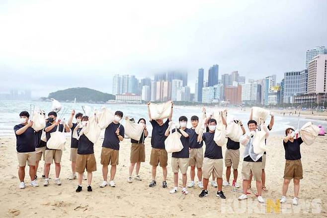 유니클로 부산 지역 직원과 한국청소년해사법학회 학생들이 가방 가득 주워 담은 쓰레기를 해운대 해변에서 들어 올리고 있다.