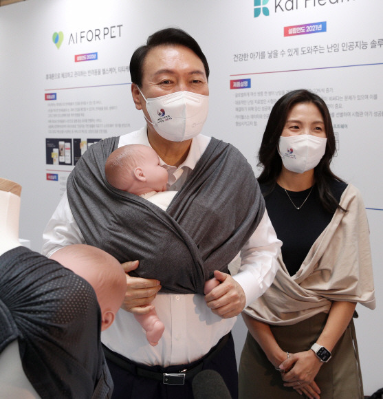 윤석열 대통령이 5일 오후 서울 여의도 중소기업중앙회관에서 제1회 여성기업주간 ‘여성경제인의 날 유공자 정부포상 수여식’에 참석하기 전 육아용품 브랜드 코니바이에린 부스에서 아기띠를 매어보고 있다. 2022. 7. 5 박지환 기자
