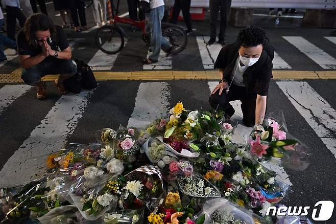 아베 신조(安倍晋三) 전 일본 총리가 총격 사망한 8일 사고 현장인 일본 나라 야마토사이다이지 역 외곽의 현장에서 시민들이 꽃을 놓는 임시 기념비 앞에서 슬퍼하고 있다. © AFP=뉴스1