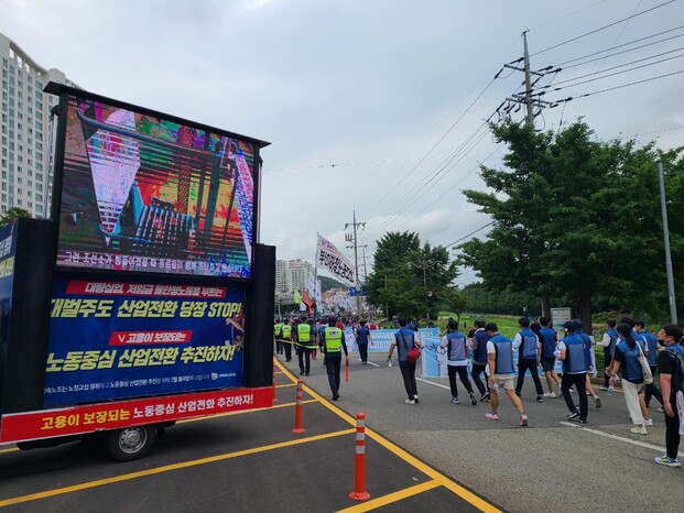 지난 8일 조선소 하청 노동자 투쟁 승리 민주노총 결의대회 참석자들이 경남 거제 대우조선해양 옥포조선소 남문에서 서문으로 행진하는 동안 유최안 부지회장이 스스로를 가둔 철제 구조물 안에서 연대를 호소하는 영상이 나오고 있다. 방준호 기자