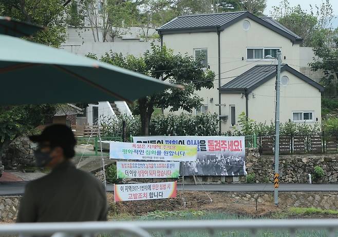 지난 14일 낮 경남 양산시 하북면 지산리 평산마을 문재인 전 대통령 사저(오른쪽 건물 뒤쪽 일부분만 보이는 건물) 앞에 ‘우리들의 평화와 일상을 돌려주세요’ ‘욕설은 자제해주세요. 평화적인 집회를 원합니다’ 등이 적힌 현수막이 걸려 있는 가운데 경호처 직원이 사저 경비를 서고 있다.  연합뉴스