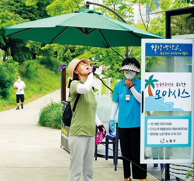 14일 오전 노원구 상계동 당현천 바닥분수 인근 산책로 입구에 ‘힐링냉장고’가 선보였다. 힐링냉장고는 노원구가 3년째 이어오고 있는 혹서기 온열질환 예방을 위한 무료 생수 나눔 사업으로 설치됐다. 구는 올해 산책로, 하천변 등에 16대의 힐링냉장고를 두고 8월31일까지 매일 300㎖ 생수 6만7천 개를 공급한다. 자원봉사자 김미례(오른쪽)씨가 힐링냉장고에서 꺼낸 생수를 시원하게 마시는 한 주민의 모습을 보고 있다.