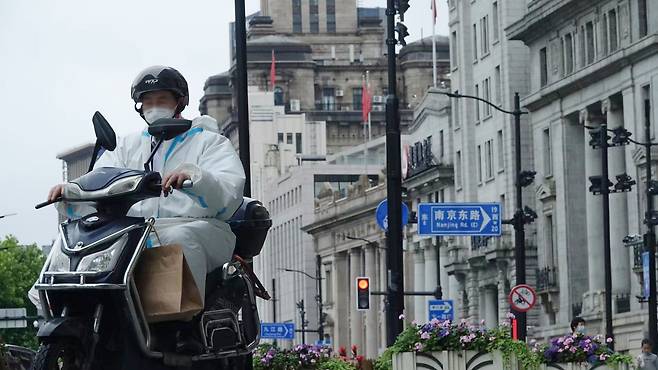 코로나19 확산으로 도시 봉쇄 조치가 내려졌던 5월 29일 중국 상하이 와이탄에서 흰 방호복을 입은 배달 기사가 오토바이로 이동하고 있다. / 연합뉴스