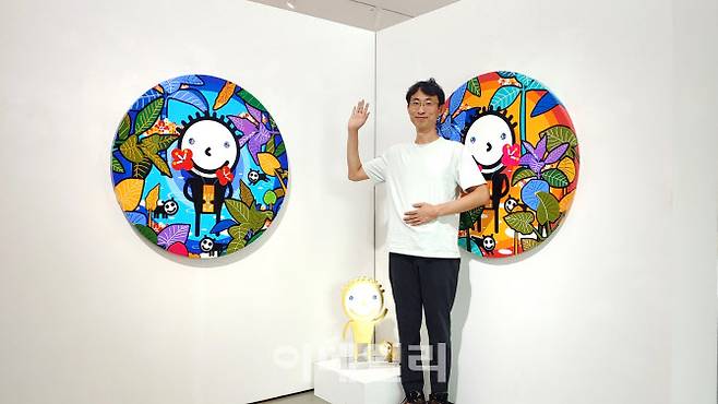 작가 권기수가 서울 성동구 아뜰리에아키서 연 개인전 ‘골든아이 속 우주’에 내놓은 자신의 작품들 사이에서 ‘동구리 포즈’를 취하고 있다. ‘눈 속 우주: 푸른 원’(The Universe in the Eye: Blue Circle·2022)과 ‘눈 속 우주: 붉은 원’(The Universe in the Eye: Blue Circle·2022) 사이에 전시작 중 유일한 조각작품 ‘무제’(2022)가 놓였다(사진=오현주 문화전문기자).