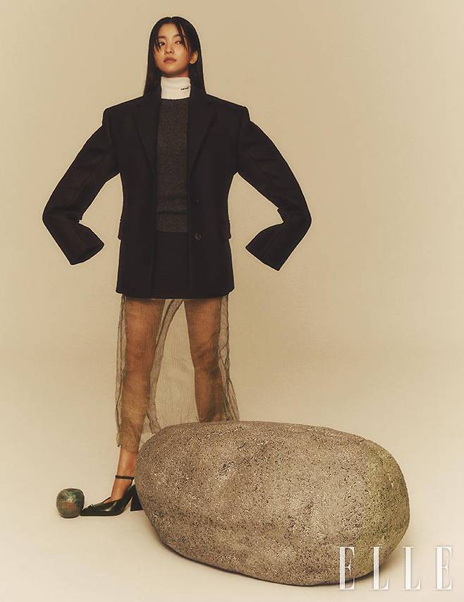 매니시한 블랙 재킷과 화이트 터틀넥 디테일의 그레이 니트 톱, 버진 울과 레이어드한 메탈릭 소재의 스커트, 블랙 메리 제인 슈즈 힐은 모두 Prada.