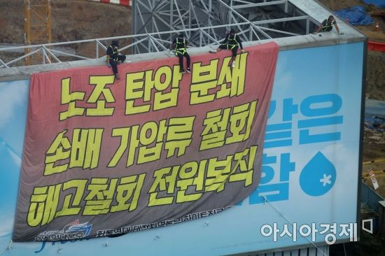 민주노총 공공운수노조 화물연대가 서울 강남구 하이트진로 본사를 점거한 채 사흘째 시위를 이어가고 있는 18일 건물 외벽에 요구사항이 적힌 현수막이 걸려 있다. 노동자들이 옥상 광고판에 올라가 고공 농성을 하고 있다. /문호남 기자 munonam@