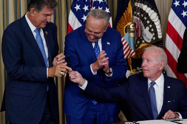 조 바이든(맨 오른쪽) 미국 대통령이 지난 16일(현지시간) 백악관 스테이트 다이닝룸에서 기후변화 대응과 의료보장 확충 등의 내용이 담긴 '인플레이션 감축법'에 서명 후 조 맨친 상원의원에게 펜을 선물하고 있다. 워싱턴=AP 뉴시스