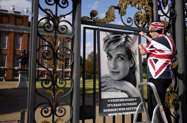 다이애나 전 영국 왕세자비의 25주기 기일을 앞두고 한 추모객이 런던 켄싱턴궁 입구에 그의 생전 모습이&nbsp;담긴&nbsp;사진을 내걸고 있다. 다이애나는 1997년 8월30일 프랑스 파리에서 교통사고로 사망했다. EPA연합뉴스