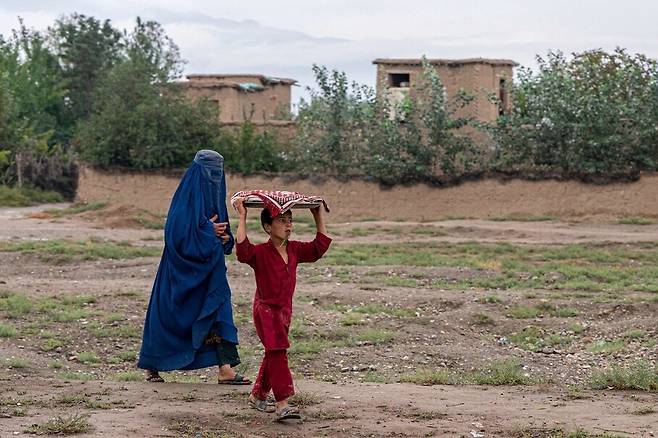 부르카를 입은 아프가니스탄 여성과 소년이 25일(현지시각) 파르완주 바그람 지역에서 걸어가고 있다. ♣파르완/AFP 연합뉴스