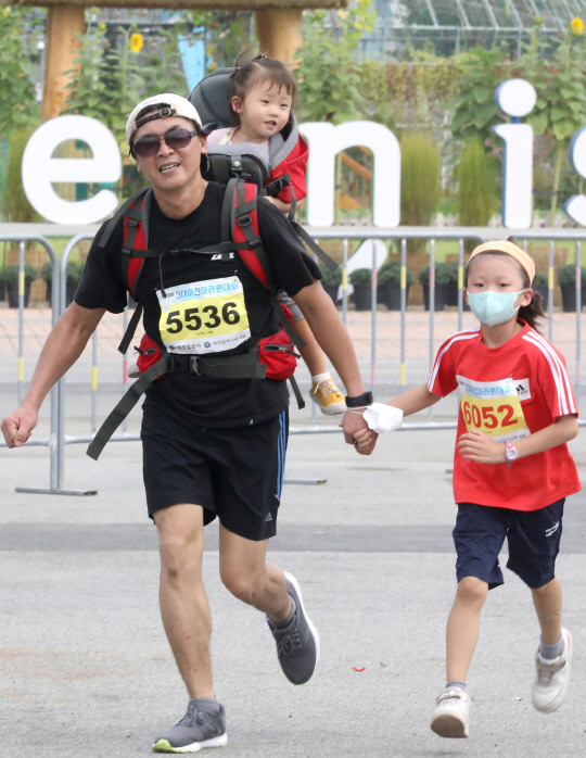 대전일보사와 대전시체육회가 공동 주최한 '제18회 3대하천마라톤대회'가 18일 엑스포시민광장에서 열려 5km 코스 주자가 아이를 업고 결승점을 향해 달리고 있다.