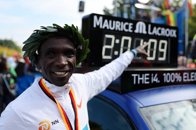 엘리우드 킵초게가 25일 독일 베를린 마라톤에서 2시간1분9초의 세계신기록을 세운 뒤 월계관을 쓰고 자신의 기록을 가르키며 기뻐하고 있다. 베를린 | AP연합뉴스